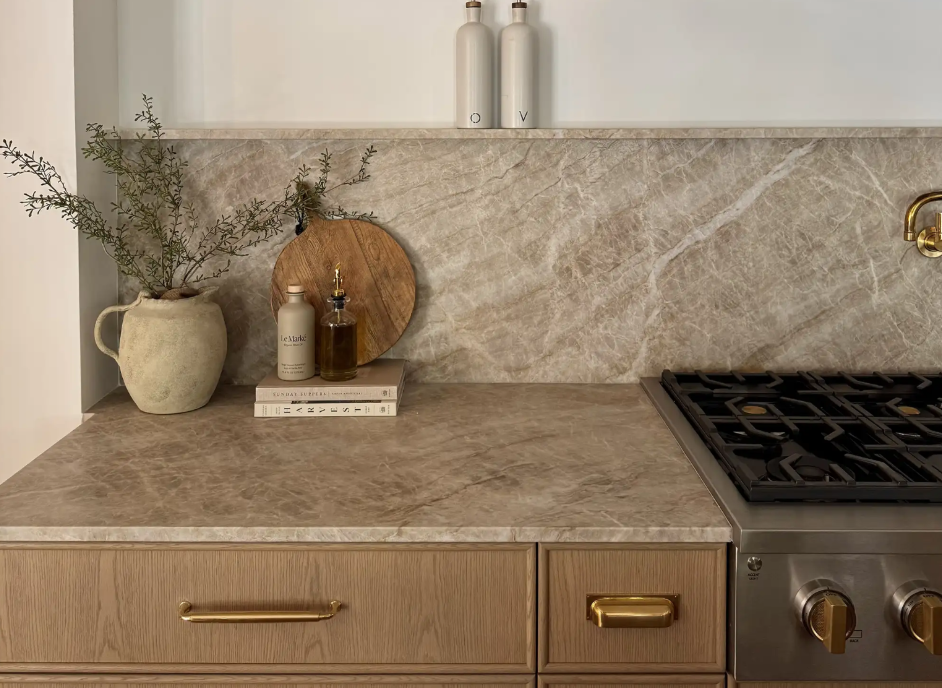 Warm taupe Taj Mahal Leather Quartzite counter and full-height backsplash with white oak cabinetry and brass fixtures.