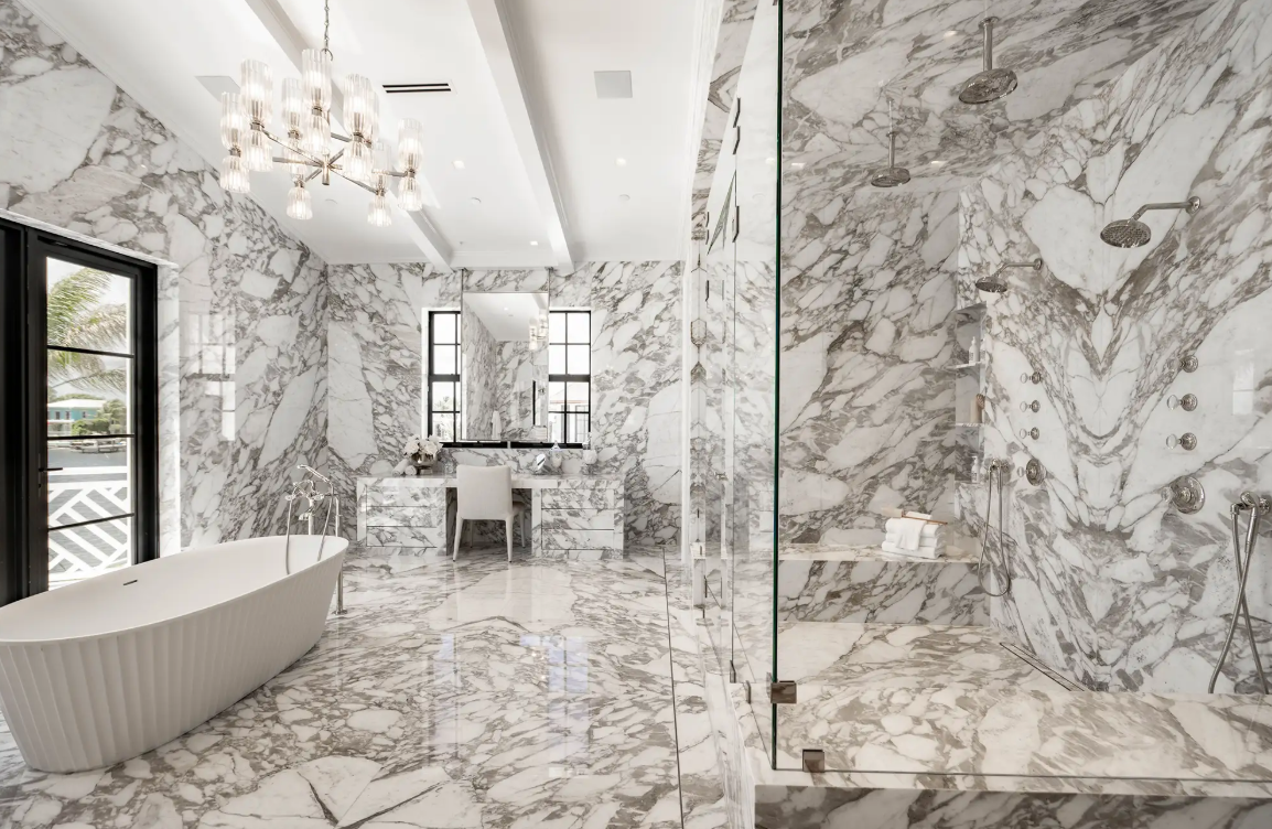 White-and-grey marble bathroom with a book-matched marble shower wall, freestanding tub, and marble floors.