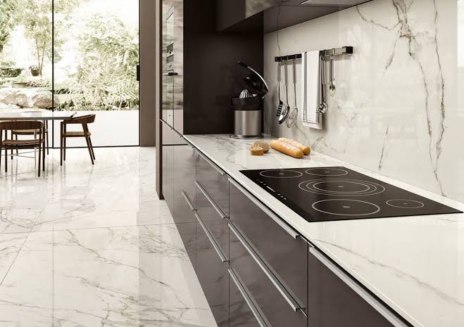 Sleek dark-cabinet kitchen with matching porcelain marble-look countertop, backsplash, and flooring, featuring an induction cooktop.